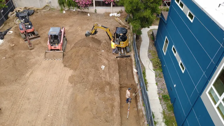 Skid steer and mini excavator backfilling and compacting a graded building pad