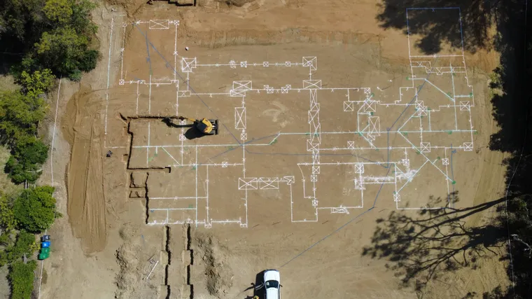 Aerial view of chalked foundation layout lines with an excavator cutting footings to the line