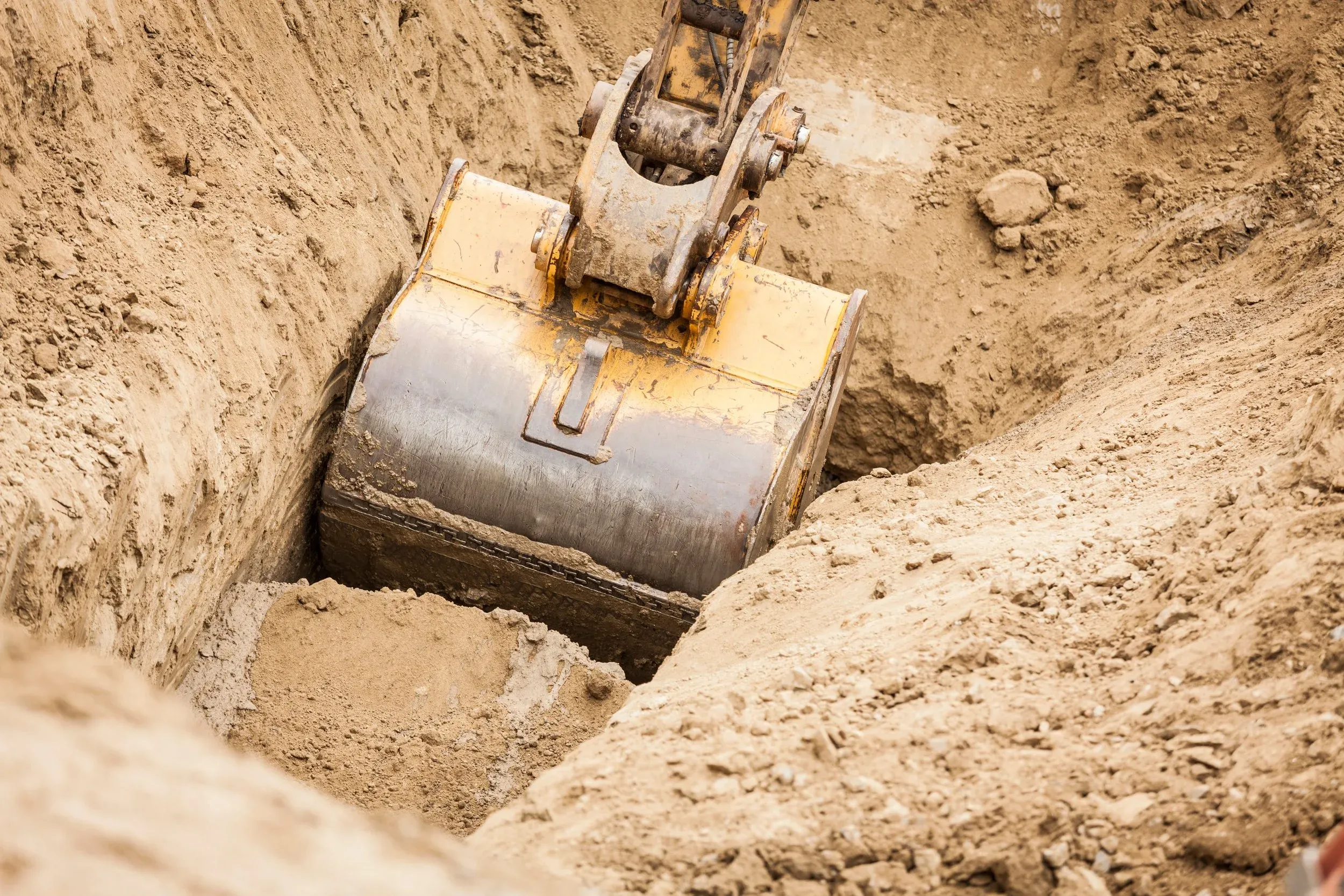 Excavator bucket digging a deep trench in compacted earth