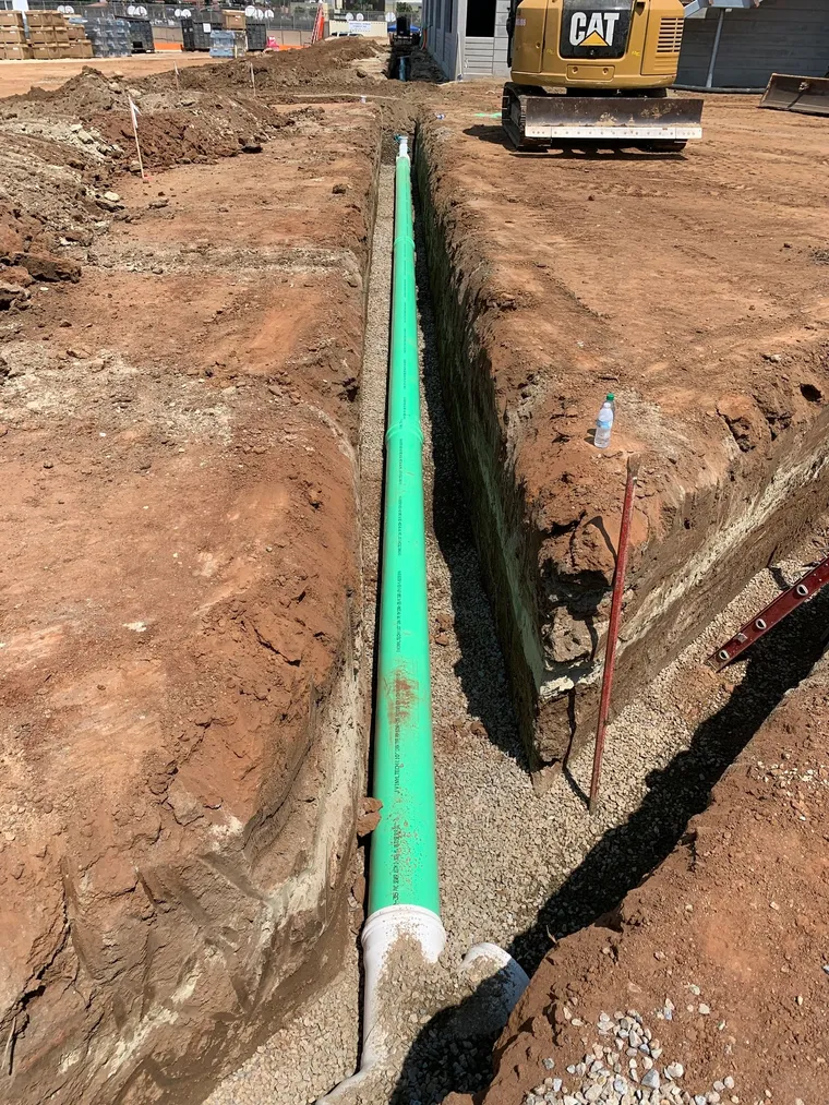 New green sewer pipe installed in an open trench alongside a concrete structure