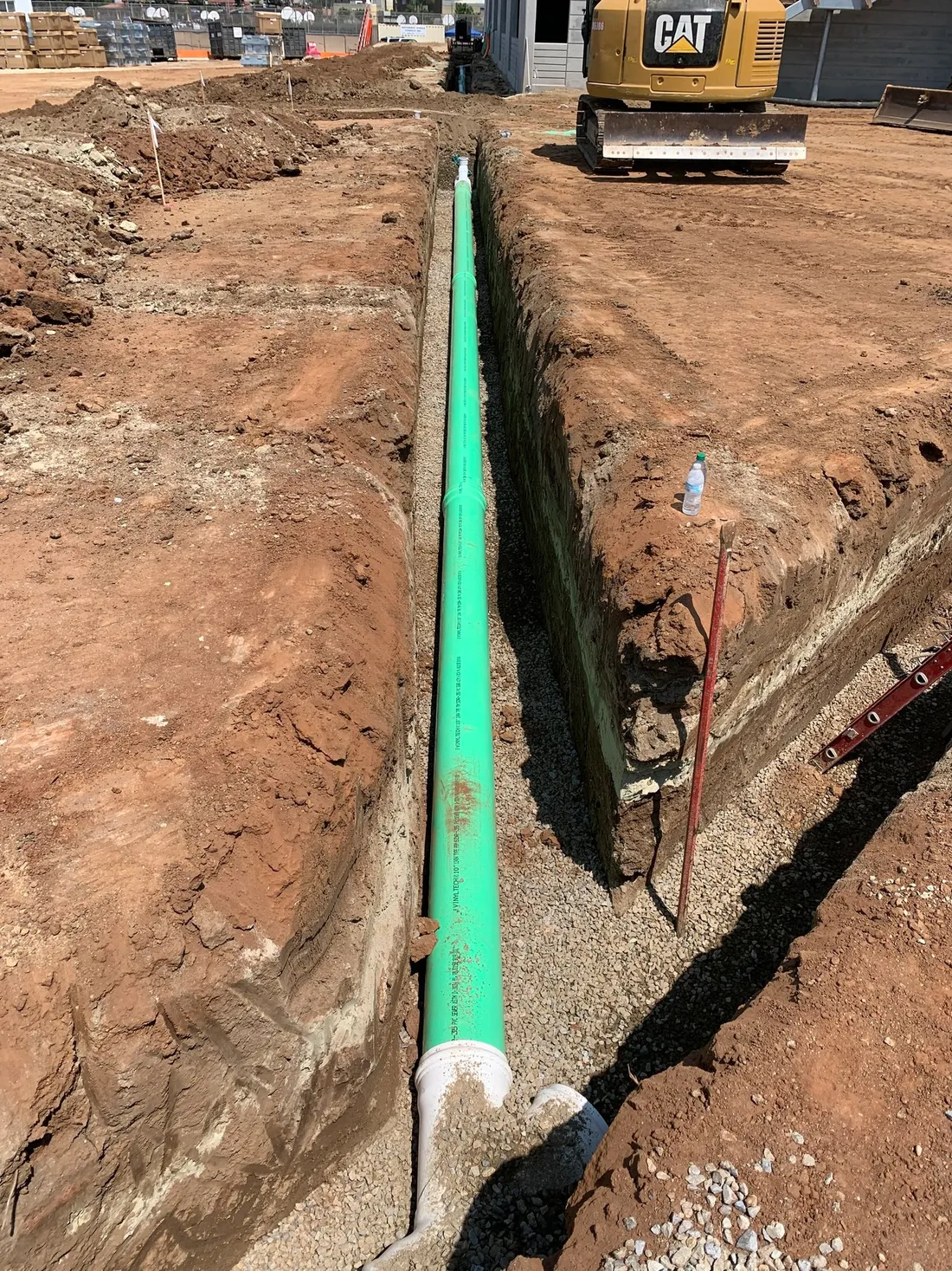 New green sewer pipe installed in an open trench alongside a concrete structure