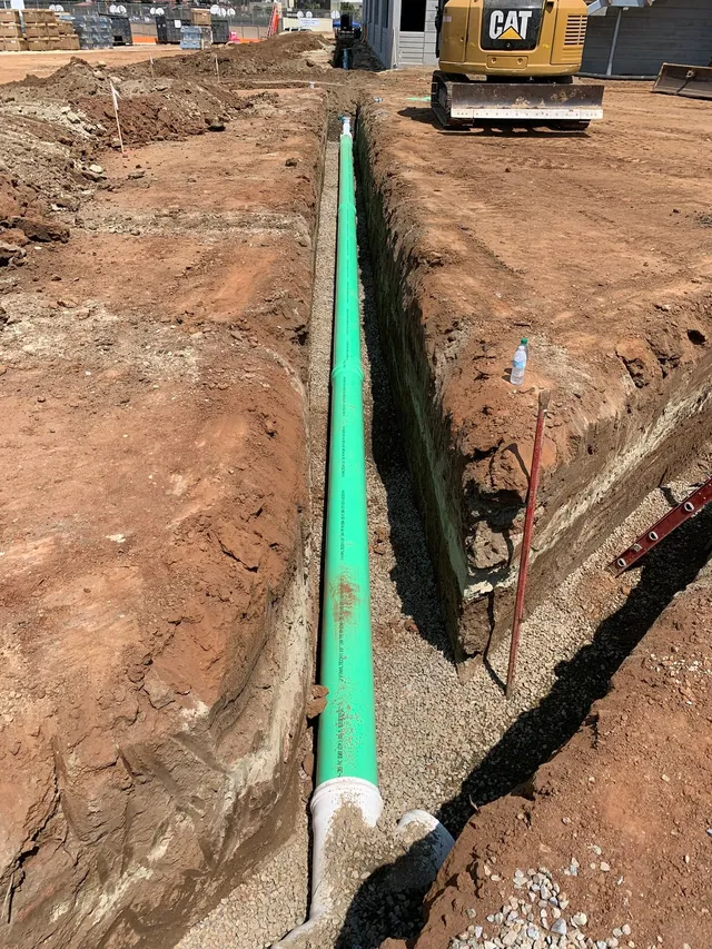 New green sewer pipe installed in an open trench alongside a concrete structure