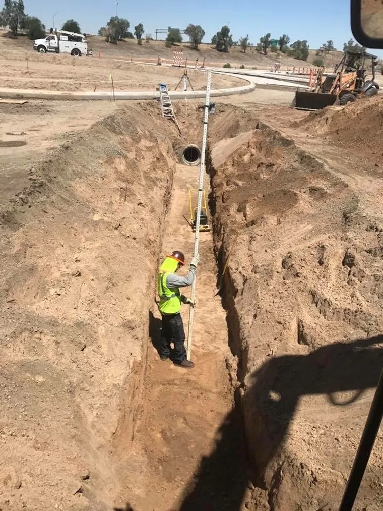 Crew member installing a water line riser in an open utility trench
