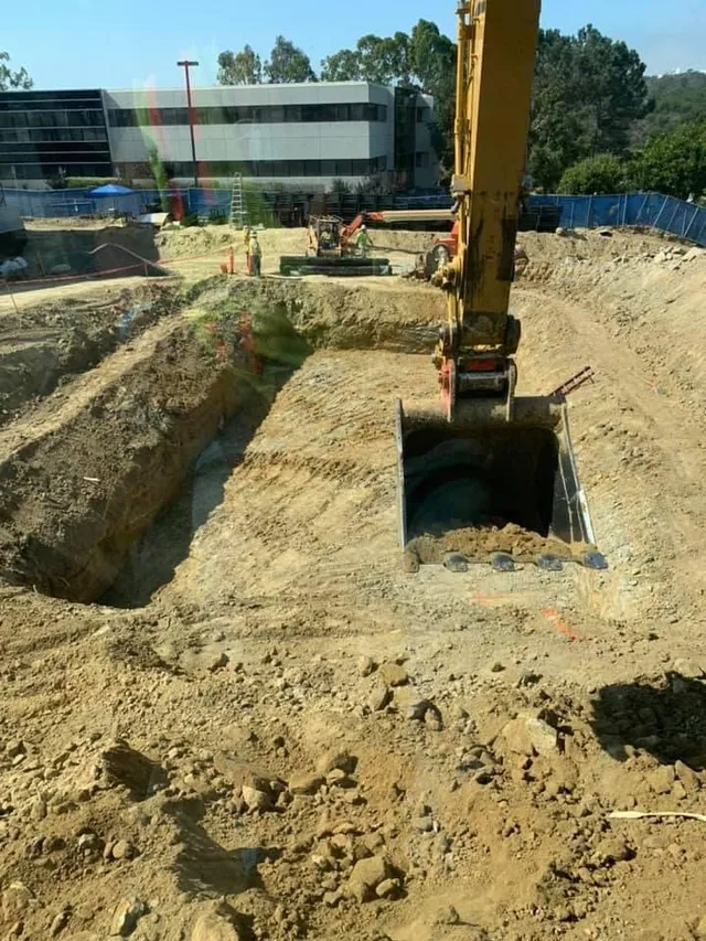 Excavator bucket digging a precise foundation pit on a commercial construction site