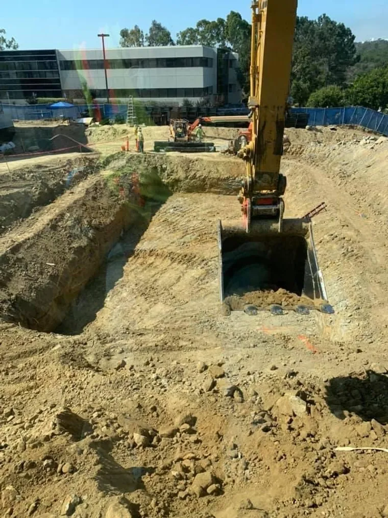 Excavator bucket digging a deep foundation pit on a commercial site