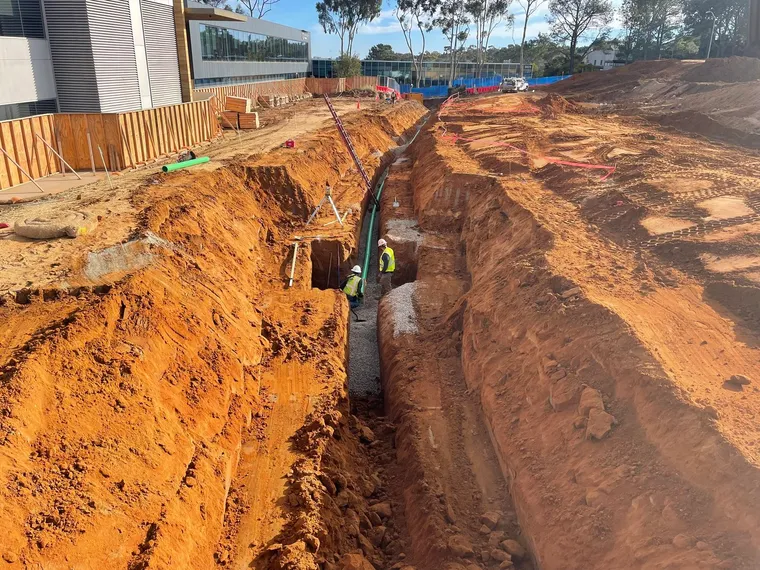Deep utility trench with crew installing conduit in Southern California soil