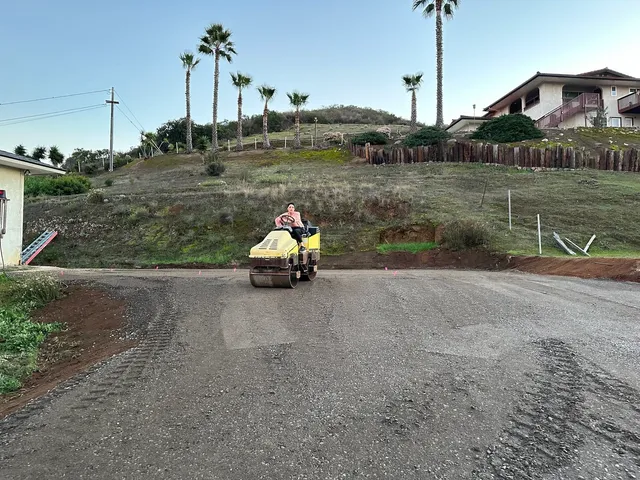 Roller compacting a gravel pad on a hillside property