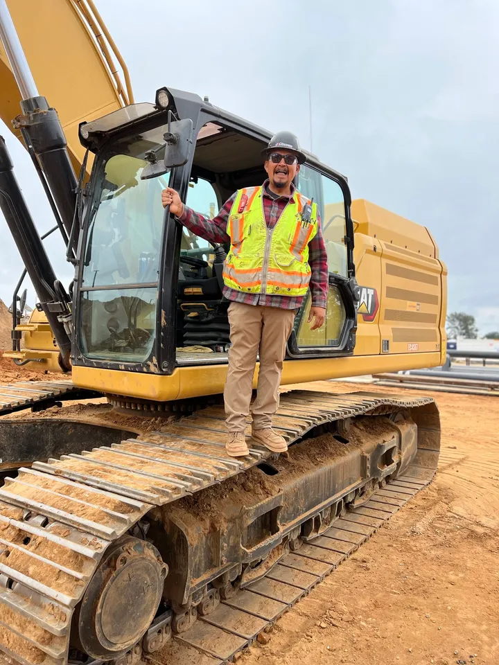 Andres standing on the tracks of an excavator in a safety vest and hard hat