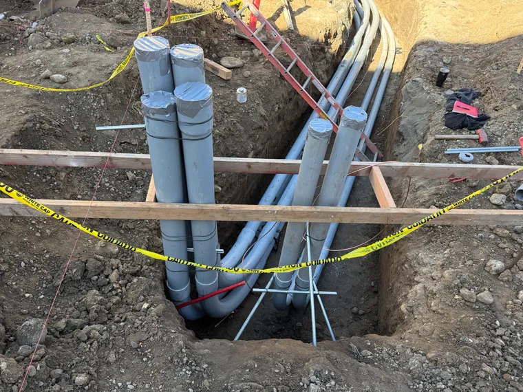 Primary conduit sweeps rising from a duct bank trench, staked and taped for inspection